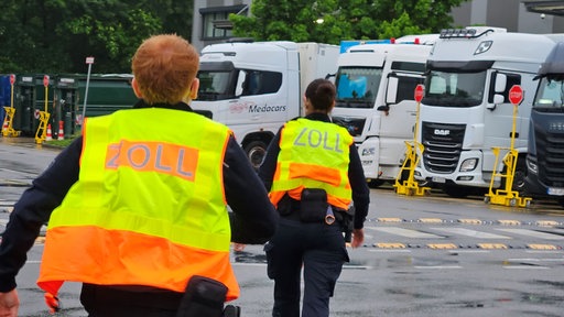 Zwei Beamte der Zollfahnund laufen im Rahmen einer Konrolle im Rheinland auf eine Reihe von geparkten Lkw zu