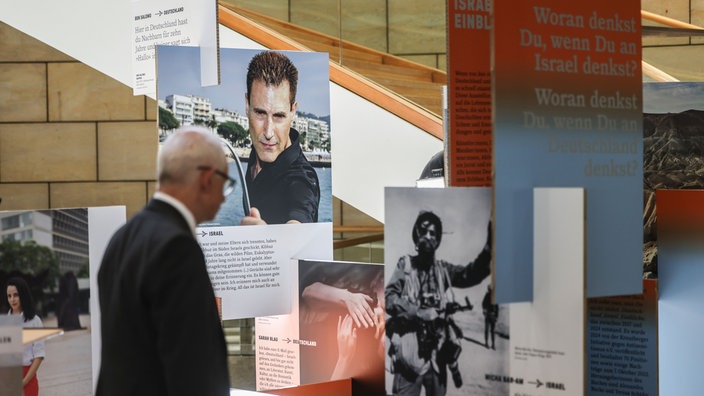 Mann steht vor Ausstellung "Deutschland. Israel. Einblicke" und bewundert die Ausstellung. Er steht im NRW Landtag und trägt einen schwarzen Anzug.