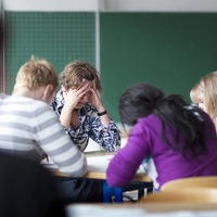 Lehrerin sitzt erschöpft mit Schülern am Tisch