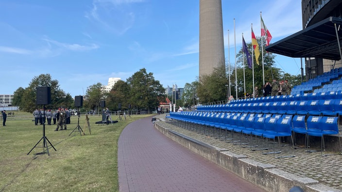 Tribüne vor NRW Landtag mit blauen Sitzen, im Hintergrund der Fernsehturm, Auf der Wiesen sind Lautsprecher aufgebaut und Rekruten laufen in Uniform über die Wiese