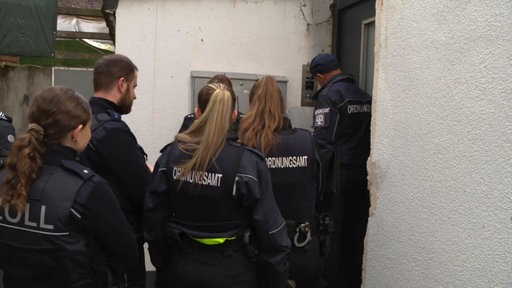 Mitarbeitende von Ordnungsamt und Zoll stehen vor einer Schrottimmobilie in Hagen.
