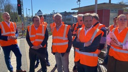Mehrere Männer in roten Warnwesten stehen auf einem Bahnsteig, zweiter von links: NRW-Verkehrsminister Oliver Krischer