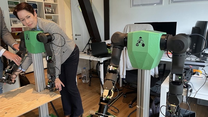 Ministerin Gorißen gibt einem Roboter Nachhilfe beim Packen von Kisten