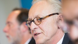 Martin Renner spricht. Rechts und Links von ihm sind verschwommen zwei weitere Männer zu sehen.