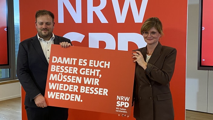 Sarah Philipp und Frederick Cordes bei einem Pressetermin mit einem Schild zur Kampagne "Wir haben verstanden."