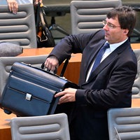NRW-Finanzminister Marcus Optendrenk wuchtet auf der Regierungsbank einen schweren schwarzen Aktenkoffer über die Sitzreihe. Aufnahme aus der Plenarsitzung am 23.08.2023