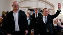 Jochen  Ott und Boris Pistorius betreten einen Raum, begleitet von weiteren Personen. Pistorius hebt eine Hand und winkt.