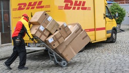 Ein Paketzusteller hat viele Päckchen auf einer Karre und liefert sie aus.