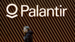 Name und Logo des Softwareunternehmens Palantir an einer Wand, im Vordergrund läuft ein Mensch vorbei