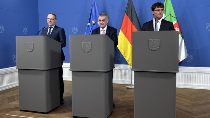 Die drei männer in Anzügen Limbach, Reul und Optendrenk bei einer Pressekonferenz