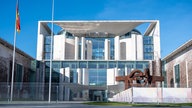 Das Kanzleramt in Berlin, links hängt eine Deutschlandfahne, der Himmel ist strahlend blau.