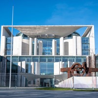 Das Kanzleramt in Berlin, links hängt eine Deutschlandfahne, der Himmel ist strahlend blau.
