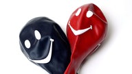 Zwei Luftballons in schwarz und rot, nicht aufgeblasen, mit weißen Smiley-Gesichtern