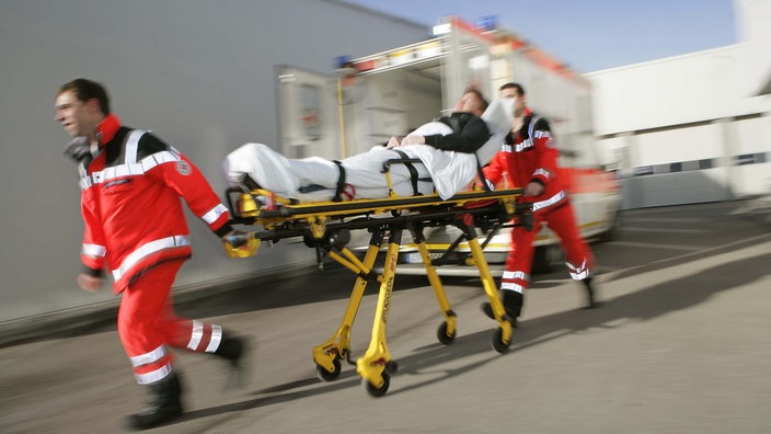 Zwei Sanitäter ziehen eine Trage mit einem Patienten drauf.