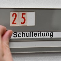 Zwei Hände befästigen ein Schild an der Wand mit der Aufschrift: Schulleitung und der Nummer 25 