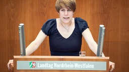 Verena Schäffer im NRW-Landtag. Sie steht am Rednerpult und spricht. Hände aufgestützt.