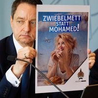 Jürgen Kayser (l), Leiter des NRW-Verfassungsschutzes, und NRW-Innenminister Herbert Reul (CDU) bei der Vorstellung des NRW Verfassungsschutzberichts 2025. Kayser hält dabei ein Plakat mit einem KI Bild aus dem Rechten Spektrum.