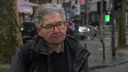 Rechtsanwalt Michael Biela-Bätje schaut ernst in die Kamera, im Hintergrund verschwommen Kölner Innenstadt
