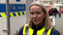 Mirella Turrek in Polizeiuniform, im Hintergrund Polizeianhänger mit mobiler Kamera und Wochenmarktstände