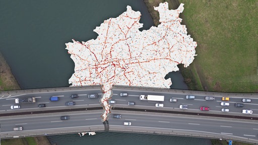 Karte von NRW mit roten und blauen Punkten, davor eine zerbrochene Brücke
