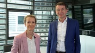 Andrea Schafarczyk und Jörg Schönenborn in einem Büroraum. Sie lächeln in die Kamera.