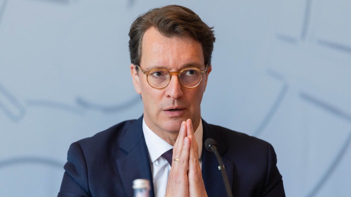 Ministerpräsident Hendrik Wüst spricht mit konzentriertem Blick in ein Mikrofon, die Hände vor dem Körper zusammengelegt.