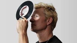 Produzent Captain Planet: Ein blonder Mann schaut durch das Loch einer Single mit Lichtpunkt auf seinem Auge