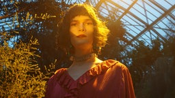 Musikerin Lucy Liebe in einem roten Kleid im Gegenlicht in einem Gewächshaus