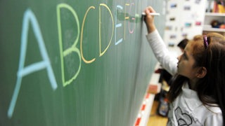 Ein Mädchen schreibt das ABC auf eine Schultafel