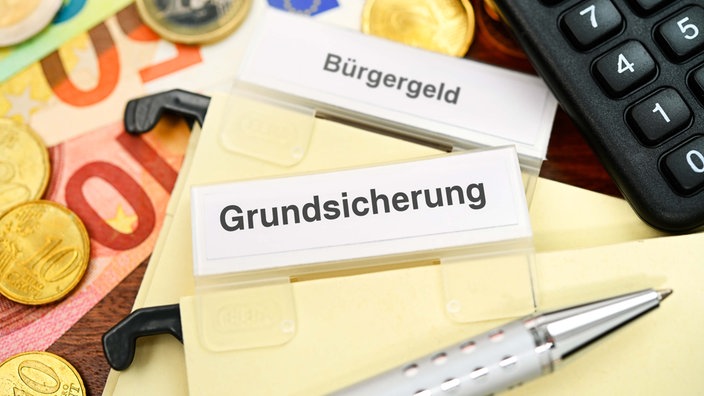 novac, kalkulator i kartice sa natpisom "Bürgergeld" i "Grundsicherung".