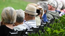 Rentner und Rentnerinnen, auf einer Bank sitzend, von hinten fotografiert