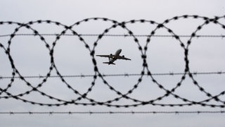 Ein Flugzeug im Himmel durch einen Stacheldraht gesehen