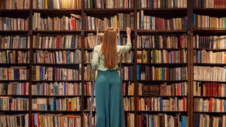 Junge Frau sucht ein Buch aus einer Bücherwand aus