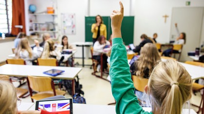 Schule, Symbolfoto: Kind hebt im Unterricht die Hand