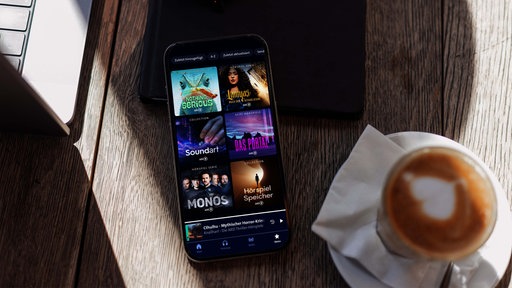 ein Smartphone auf einem Tisch, das die Hörspiele in der ARD Sounds App durchsucht.