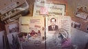 Eine Draufsicht auf einen aufgeschlagenen Ordner mit verpixeltem Portrait-Foto, Dokumenten und Zeitungsseiten. Daneben liegen verstreut Fotos, Zigarettenasche und ein Aschenbecher.