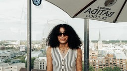 Frau Beji auf einer Dachterrasse; im Hintergrund ein Blick über eine Stadt