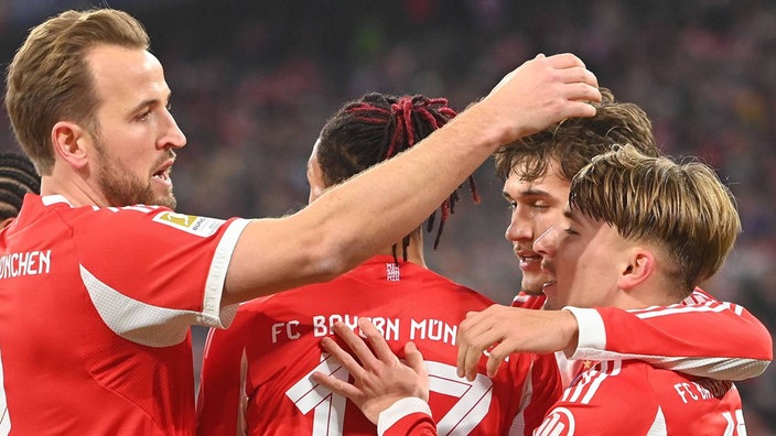 Spielszene: vier Münchener Spieler freuen sich, v.l.n.r.: Harry Kane, Michael Olise, Tom Bischof und Lennart Karl, alle in Rück- oder Seitenansicht des Oberkörpers, mit Arm oder Hand am Nachbarn