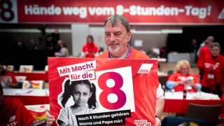 Auf dem 23. Ordentlichen Bundeskongress Deutscher Gewerkschaftsbund DGB hält ein Delegierte ein Schild mit der Aufschrift "Mit Macht für die 8 - Nach 8 Stunden gehören Mama und Papa mir!"