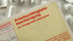 Eine Arbeitsunfähigkeitsbescheinigung zur Vorlage beim Arbeitgeber liegt auf verschiedenen Tabletten in Verpackungen