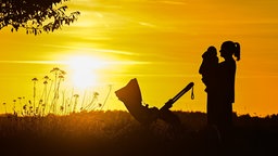 Symbolbild Mutterschaft: Eine Mutter steht mit ihrem Baby im Arm im Sonnenuntergang auf einem Feldweg (Archivfoto vom 9.10.2022)
