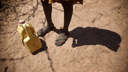 Neben den Füßen eines Nomaden in Kenia steht ein Wasserkanister