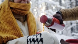 In einem verschneiten Wald gießt ein Mann einer Frau heißen Tee aus einer Thermosflasche in eine Tasse