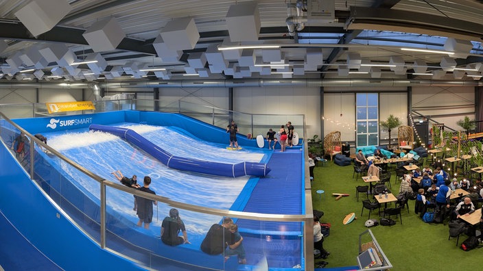 Mehrere Menschen surfen in Pinkys Surfhouse, während andere an Tischen sitzen