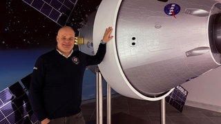 Ingenieur Tobias Langener vor einem verkleinerten Modell des Raumschiffs der "Artemis 2" Mission