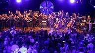 Blick auf die Bühne bei der WDR 2 Hausparty in Siegburg. Dort sitzt das Ensemble des WDR Funkhausorchesters. Von der Decke hängt eine Discokugel