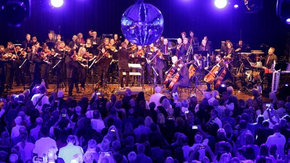 Blick auf die Bühne bei der WDR 2 Hausparty in Siegburg. Dort sitzt das Ensemble des WDR Funkhausorchesters. Von der Decke hängt eine Discokugel