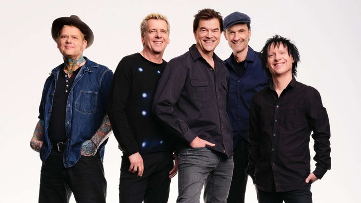 Die Toten Hosen stehen zusammen in einem leeren Raum und lächeln in die Kamera