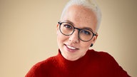 Die Sängerin Stefanie Heinzmann steht vor einem beigen Hintergrund und lächelt in die Kamera.
