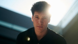 Eine Nahaufnahme von Wincent Weiss lächelnd vor einer weißen Wand